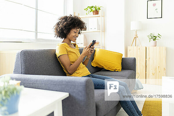 Happy woman text messaging through mobile phone on sofa at home