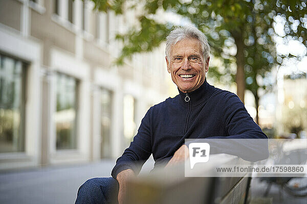 Smiling elderly man sitting on bench in park