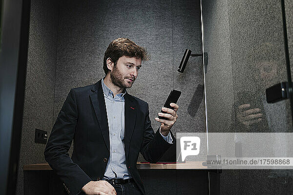 Businessman surfing net on mobile phone sitting at desk in cabin