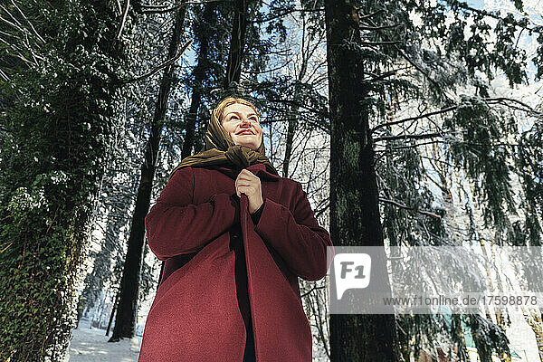 Lächelnde reife Frau  die vor Bäumen im Winterwald steht