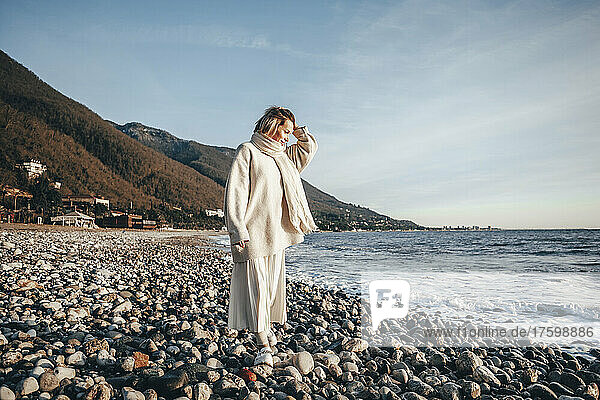 Frau mit der Hand im Haar läuft auf Steinen am Strand