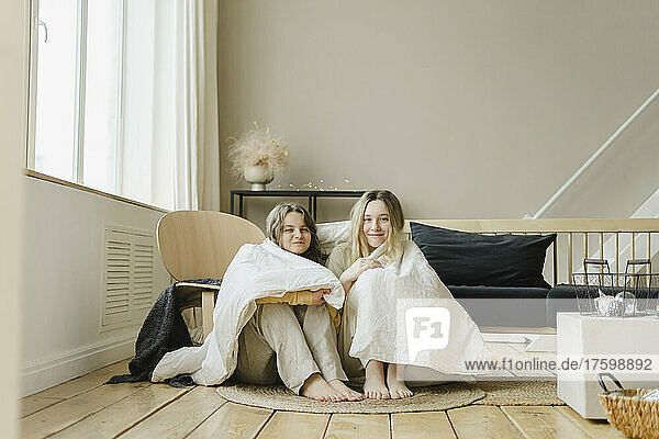 Friends wrapped in blanket at home