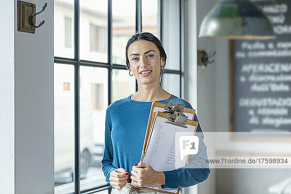 Smiling cafe owner with menu on clipboards in coffee shop