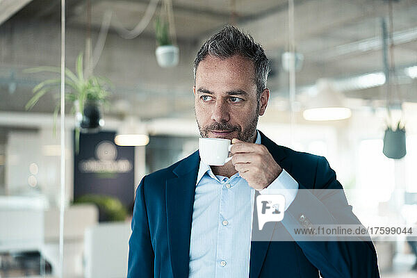 Thoughtful businessman drinking coffee at workplace