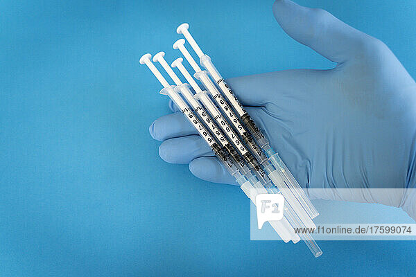 Doctor holding syringes against blue background in studio