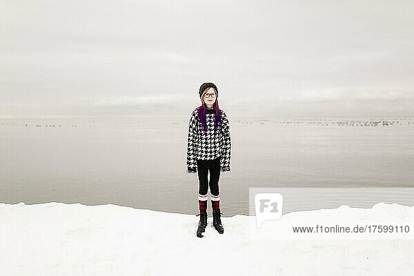 Girl wearing eyeglasses standing by lake in winter