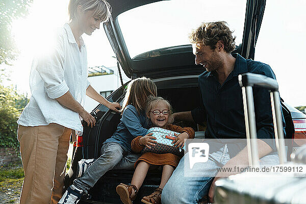 Eltern schauen Sohn zu  wie er Tochter im Kofferraum eines Autos umarmt