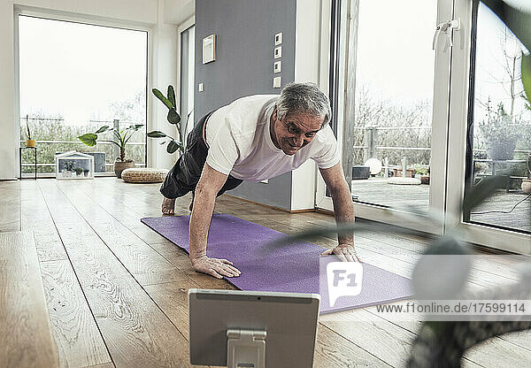 Senior man watching online tutorial doing push-ups at home