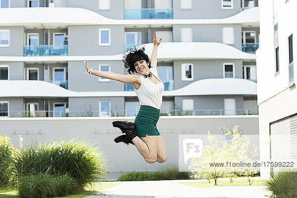 Cheerful woman jumping in front of building on sunny day