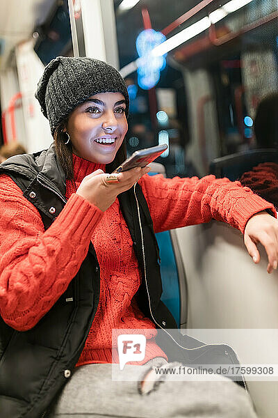 Cheerful young woman talking through mobile phone speaker in tram