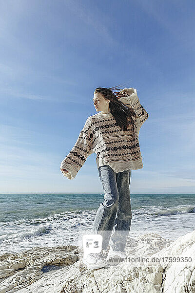 Teenage girl in sweater standing on rock at beach