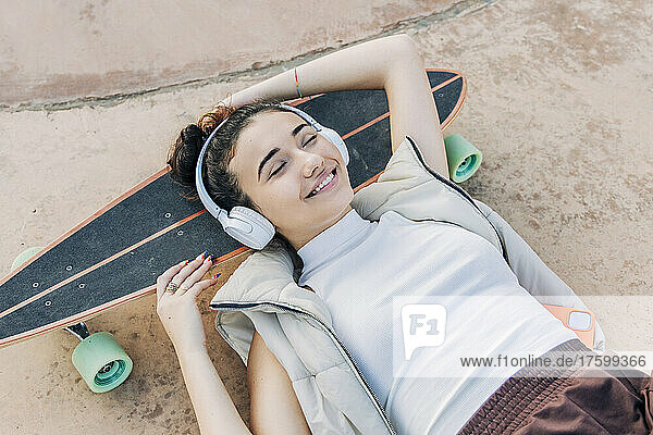 Smiling woman with headphones relaxing on skateboard in park