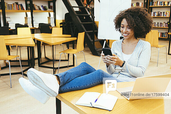 Lächelnde Geschäftsfrau  die am Schreibtisch im Kreativbüro SMS auf dem Smartphone schreibt