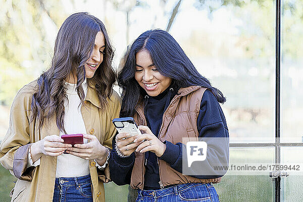 Smiling young woman sharing smart phone with friend on campus