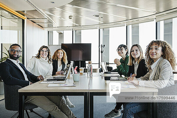 Lächelnde Geschäftsleute und Geschäftsfrauen sitzen bei einer Besprechung am Konferenztisch