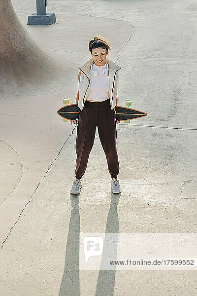 Smiling woman holding skateboard on sports ramp in park