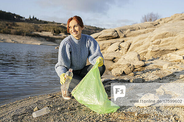 Smiling volunteer picking up plastic bottle at seashore