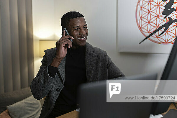 Smiling young businessman talking on mobile phone at home working late night
