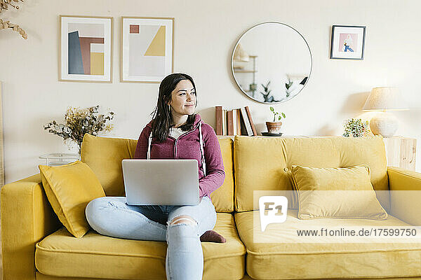 Frau mit Laptop sitzt zu Hause auf dem Sofa
