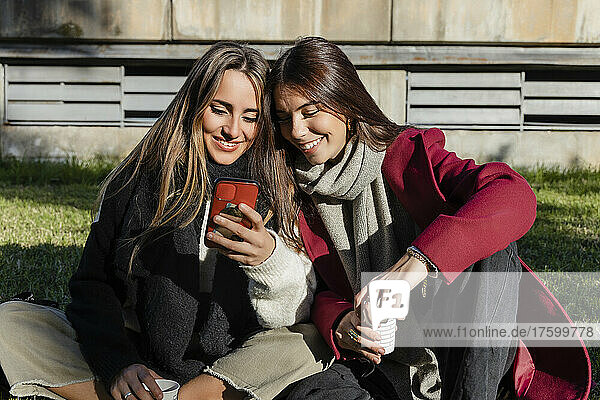 Smiling woman sharing smart phone to friend sitting together