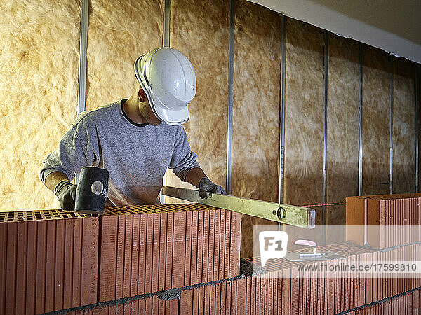 Bricklayer with hammer using spirit level on bricks at construction site