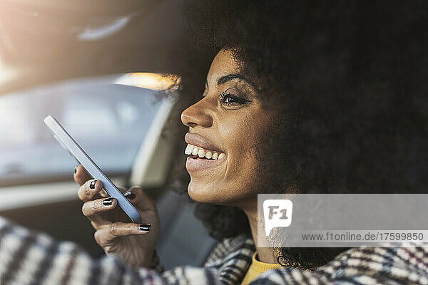 Lächelnde Frau mit Smartphone sitzt am Wochenende im Auto