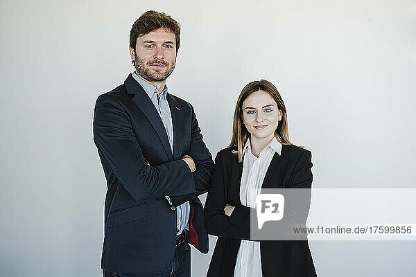 Confident businessman and businesswoman standing with arms crossed in front of wall
