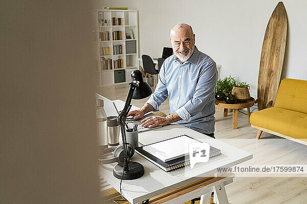 Happy freelancer with laptop sitting at desk in home office
