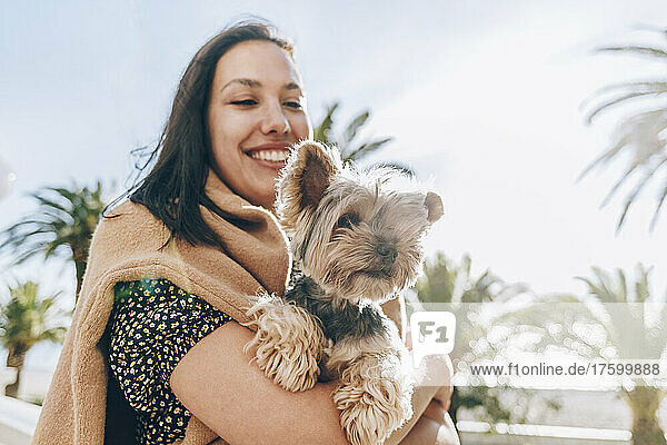Smiling woman carrying dog on sunny day
