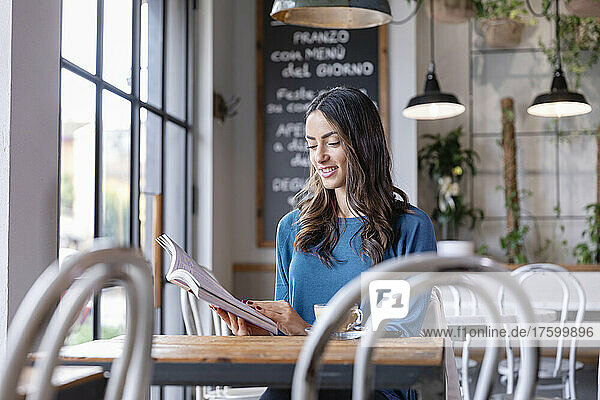 Smiling young woman reading book in illuminated cafe