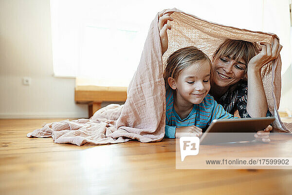 Smiling son using tablet PC with mother below shawl at home
