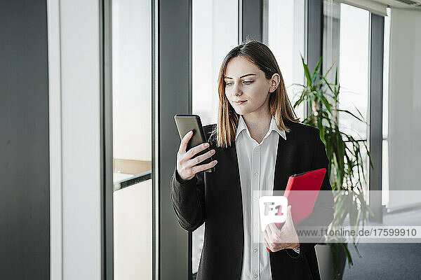 Businesswoman using smart phone holding tablet PC in office