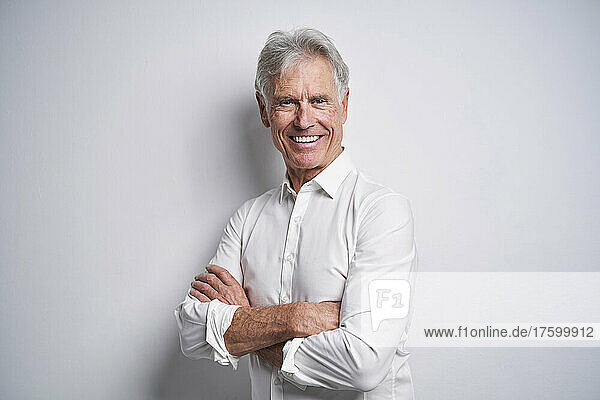 Smiling senior businessman with arms crossed in front of white background