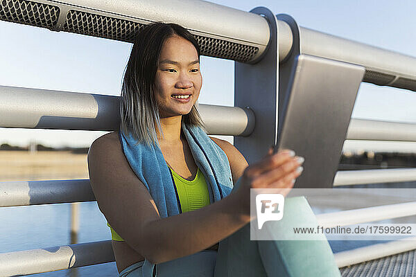 Smiling woman using tablet PC in front of railing