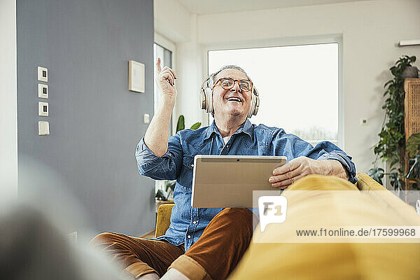 Happy senior man with eyes closed enjoying music through wireless headphones in living room