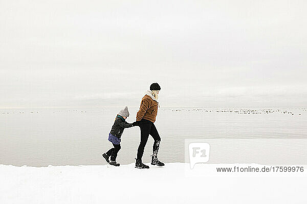 Mother and daughter walking by lake in winter