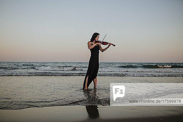 Frau spielt Geige vor klarem Himmel bei Sonnenuntergang