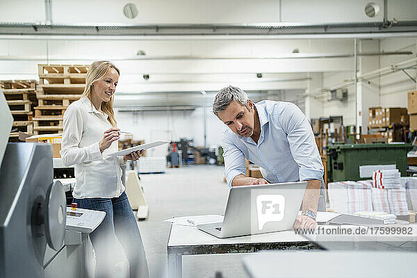 Businessman discussing ideas over laptop with colleague in factory