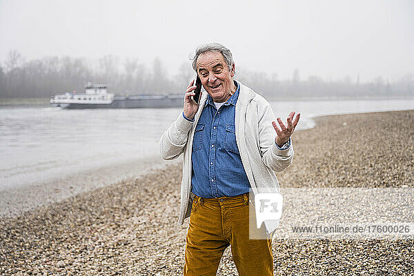 Senior man talking on mobile phone gesturing at beach