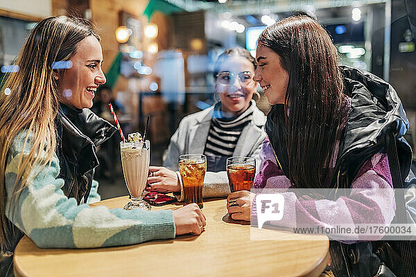 Young women with drinks on table talking in cafe