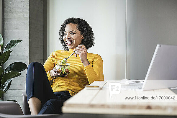 Happy businesswoman with salad bowl at work place