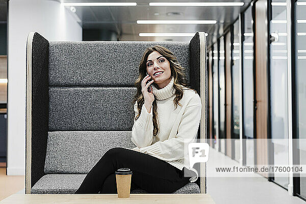 Geschäftsfrau spricht am Smartphone und sitzt am Sitz im Büro