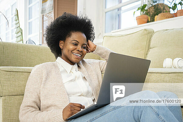 Happy freelancer using laptop by sofa in living room at home