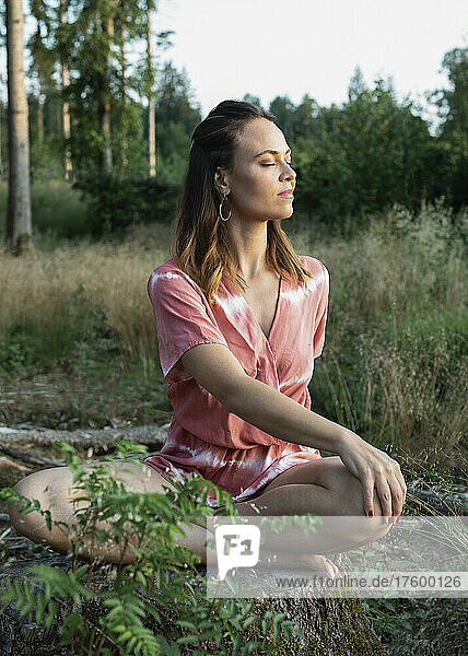 Woman meditating on tree stump in forest