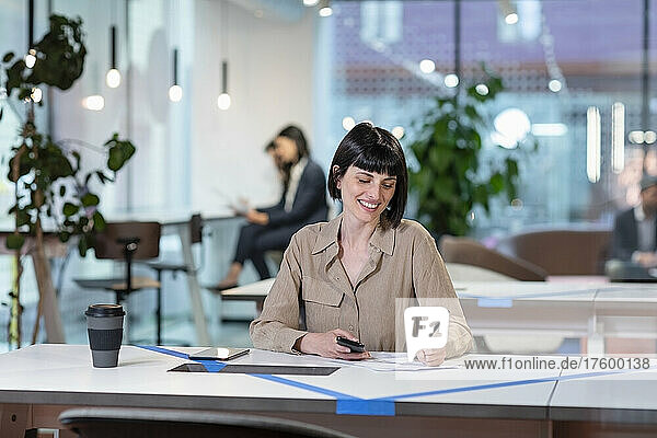 Smiling businesswoman writing on paper at table in office