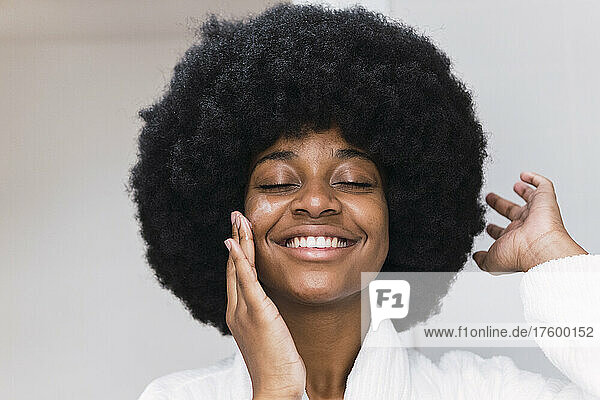 Happy young woman with eyes closed applying face cream