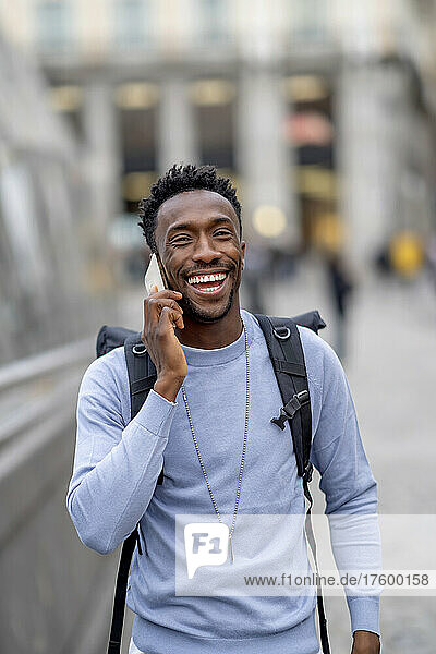 Happy young man wearing backpack talking on mobile phone