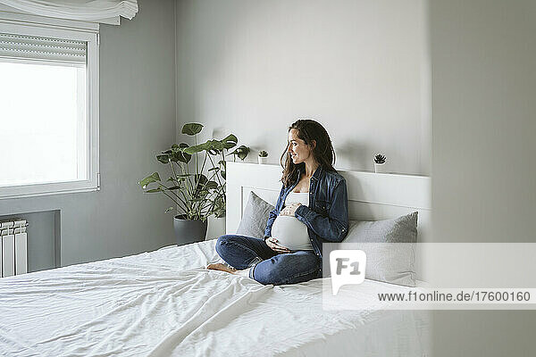 Smiling pregnant woman sitting cross-legged on bed at home