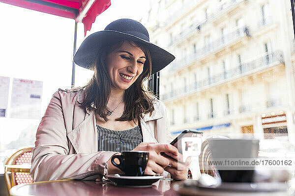 Happy young woman using smart phone sitting at cafe  Paris  France