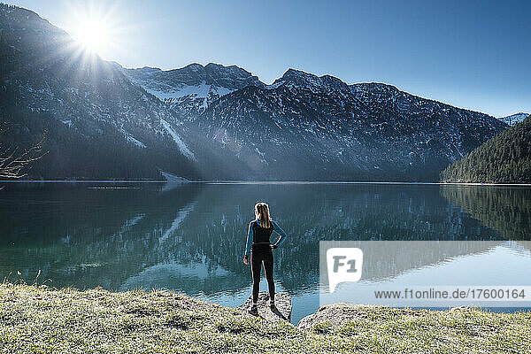 Woman with hand on hip looking across Lake Plansee to Ammergau Alps  Reutte  Tyrol  Austria
